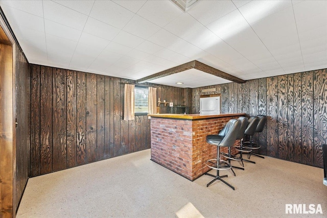 bar featuring a bar, carpet, wood walls, and freestanding refrigerator