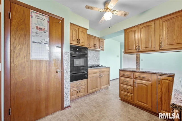 kitchen with a warming drawer, a ceiling fan, stainless steel gas stovetop, black oven, and backsplash