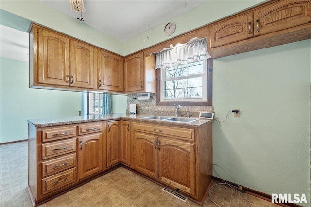 kitchen featuring a peninsula, brown cabinetry, visible vents, and a sink