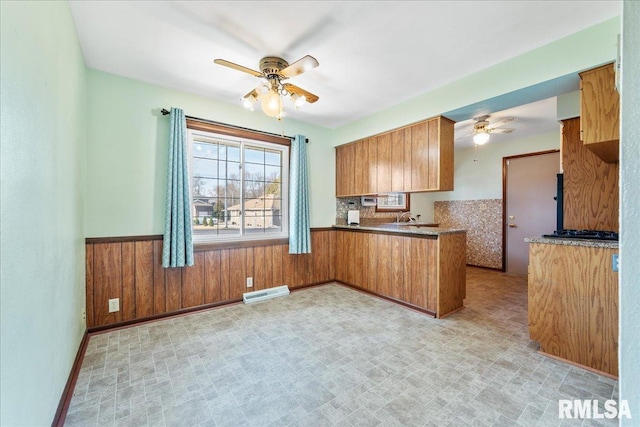 kitchen featuring brown cabinetry, visible vents, wainscoting, and ceiling fan