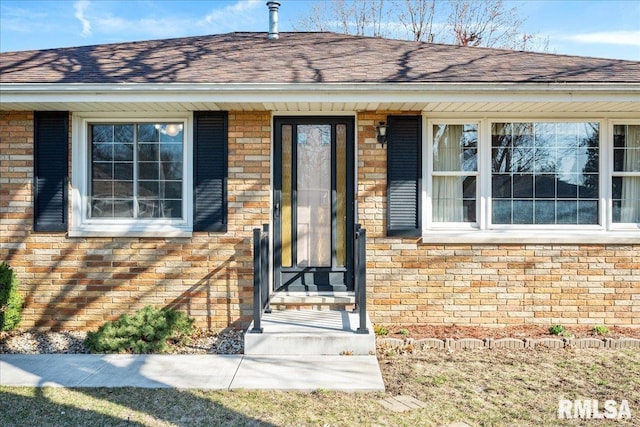 view of exterior entry featuring brick siding and roof with shingles