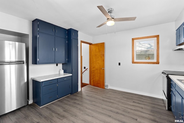 kitchen with electric stove, blue cabinetry, dark wood-style floors, freestanding refrigerator, and ceiling fan