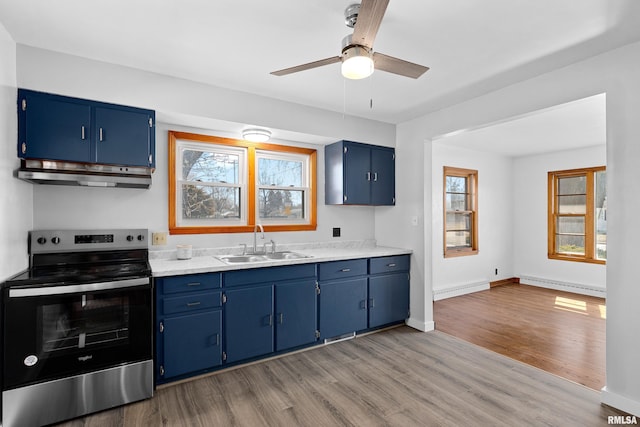 kitchen with blue cabinetry, a sink, electric stove, under cabinet range hood, and baseboard heating