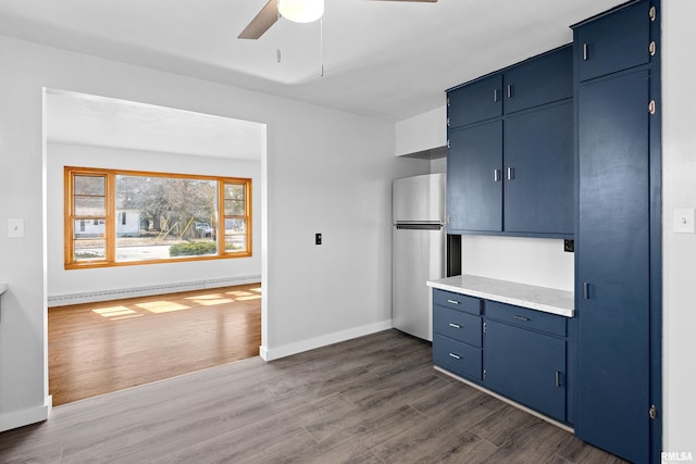 kitchen with a baseboard radiator, dark wood finished floors, blue cabinetry, freestanding refrigerator, and ceiling fan