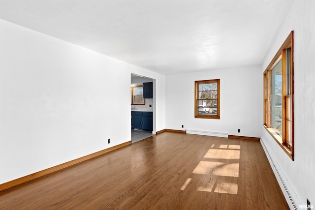 unfurnished living room featuring dark wood-style floors, baseboards, baseboard heating, and a baseboard radiator