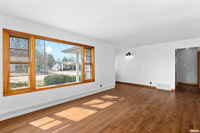 spare room featuring a baseboard heating unit, baseboards, visible vents, and dark wood-style flooring