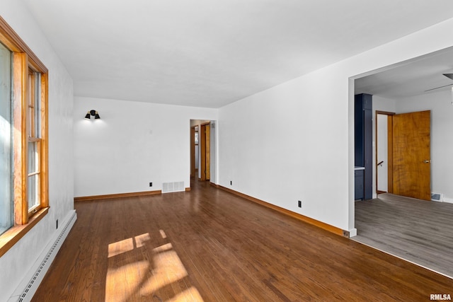 unfurnished room with a baseboard heating unit, baseboards, visible vents, and wood finished floors