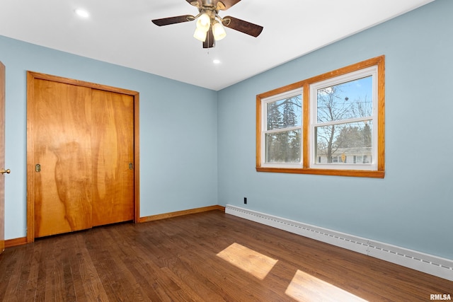 unfurnished bedroom featuring baseboards, baseboard heating, a closet, a ceiling fan, and dark wood-style flooring