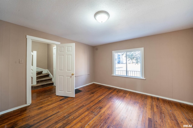 spare room with dark wood-style floors, a textured ceiling, stairs, and baseboards