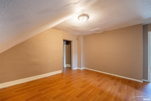 additional living space with light wood-type flooring, a textured ceiling, and attic access