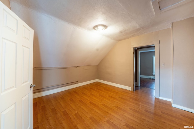 additional living space with a baseboard heating unit, vaulted ceiling, light wood finished floors, and a textured ceiling