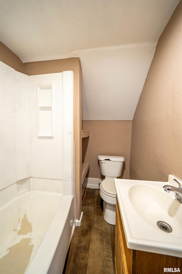 bathroom featuring vanity, wood finished floors, baseboards, lofted ceiling, and toilet