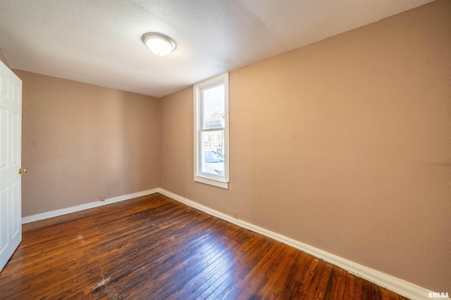 empty room with a textured ceiling, dark wood-type flooring, and baseboards