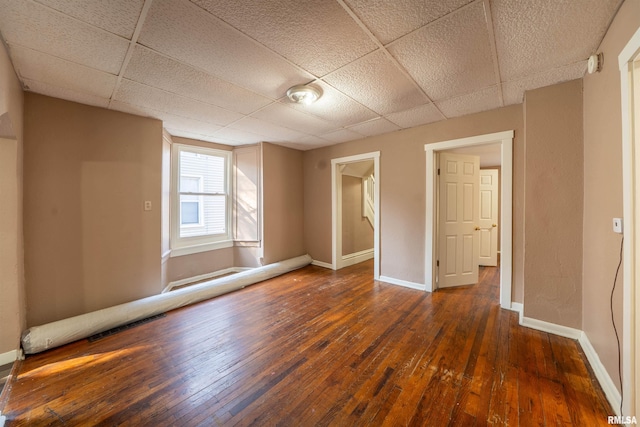 empty room with baseboards, visible vents, wood-type flooring, and a paneled ceiling