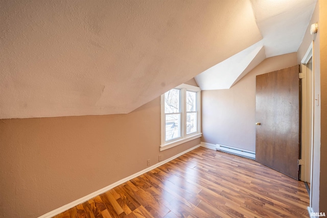 additional living space featuring wood finished floors, baseboards, lofted ceiling, a textured ceiling, and baseboard heating