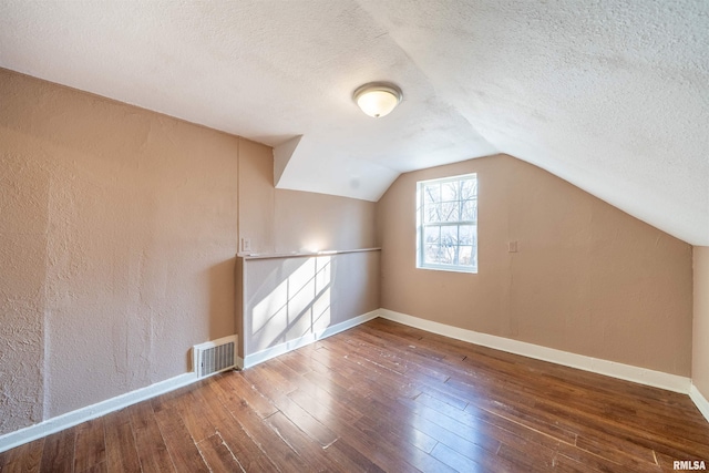 bonus room featuring visible vents, baseboards, vaulted ceiling, hardwood / wood-style floors, and a textured ceiling