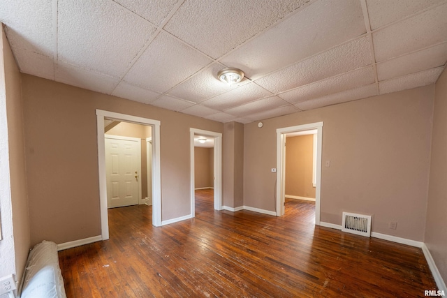 empty room featuring hardwood / wood-style flooring, baseboards, visible vents, and a paneled ceiling