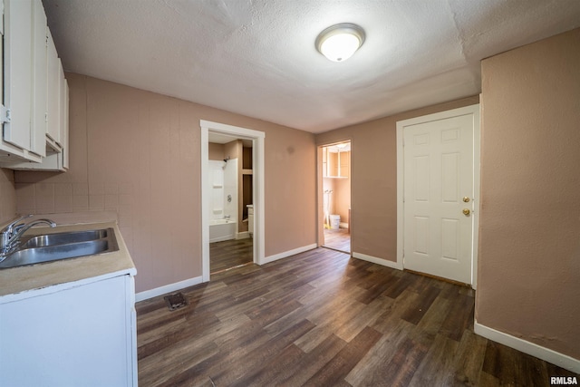 kitchen with baseboards, dark wood finished floors, a sink, light countertops, and white cabinetry