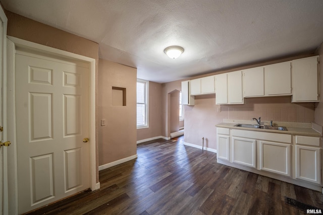 kitchen with dark wood finished floors, white cabinetry, baseboards, and a sink