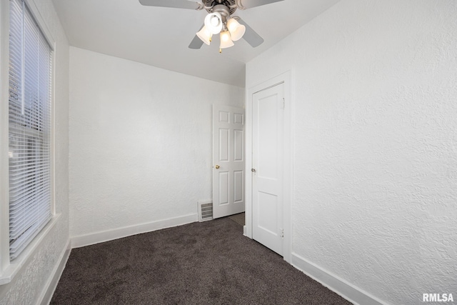 unfurnished bedroom featuring visible vents, dark colored carpet, a textured wall, and baseboards