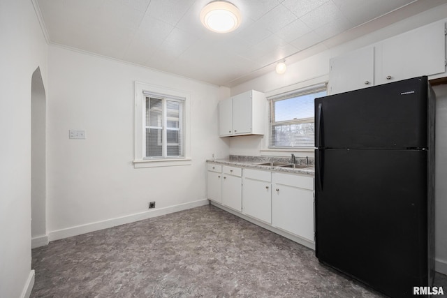 kitchen featuring baseboards, arched walkways, freestanding refrigerator, a sink, and white cabinets