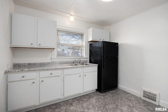 kitchen with visible vents, a sink, white cabinetry, freestanding refrigerator, and baseboards