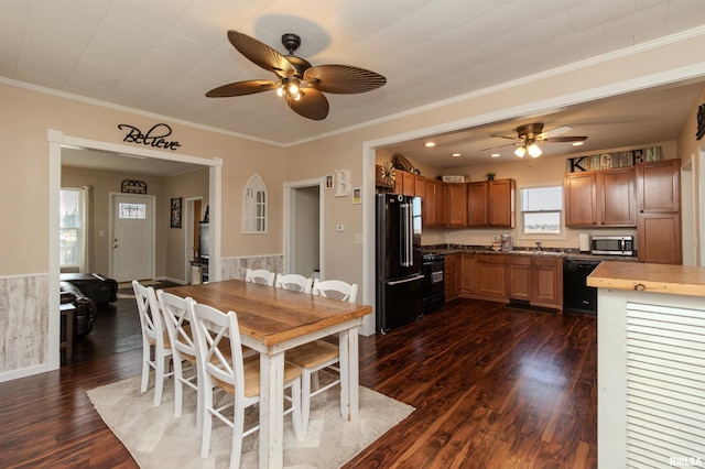 dining room with dark wood-type flooring, ornamental molding, a ceiling fan, and wainscoting