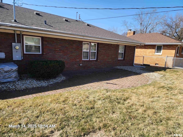 back of property featuring fence, a yard, a shingled roof, brick siding, and a chimney