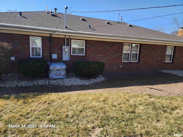 back of house with brick siding, a lawn, a chimney, and roof with shingles