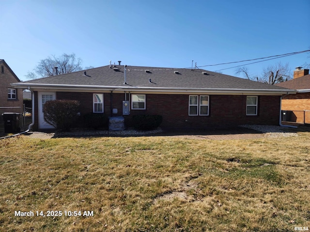 rear view of house with brick siding, roof with shingles, a yard, and fence