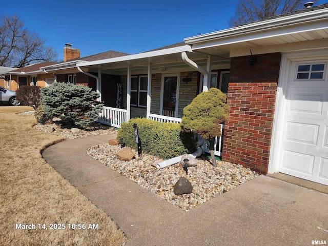 property entrance featuring brick siding, covered porch, a garage, and a chimney