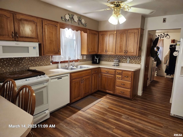 kitchen featuring brown cabinets, a ceiling fan, a sink, dark wood finished floors, and white appliances