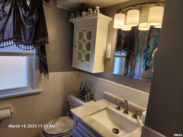 half bath featuring toilet, tile walls, wainscoting, and vanity