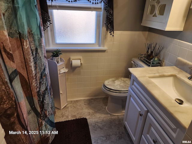 bathroom with toilet, tile walls, wainscoting, and vanity