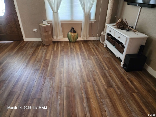 foyer entrance with a textured wall, dark wood-style flooring, and baseboards