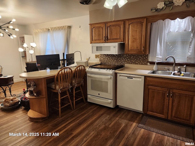 kitchen with dark wood-style floors, white appliances, a peninsula, and a sink