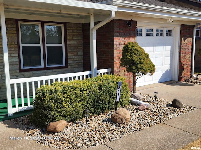 view of exterior entry with a porch, brick siding, and a garage