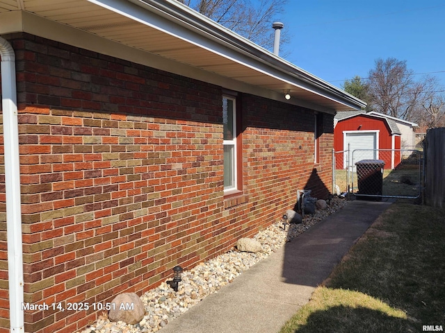 view of property exterior featuring brick siding, an outdoor structure, a shed, and fence