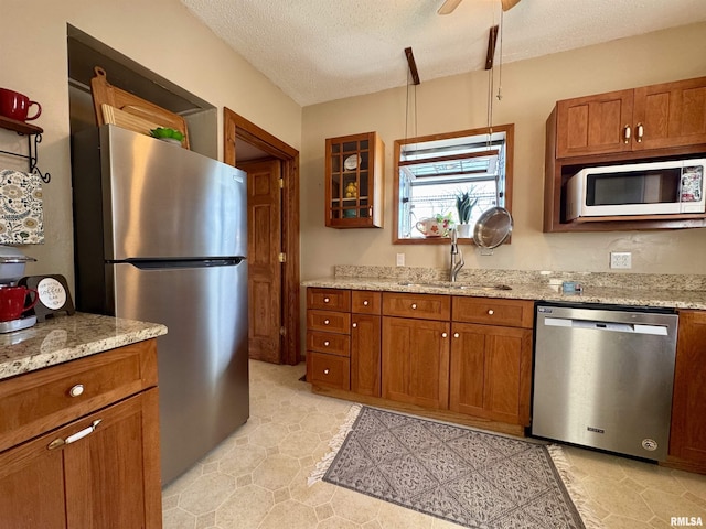 kitchen featuring light stone counters, brown cabinets, stainless steel appliances, a textured ceiling, and a sink