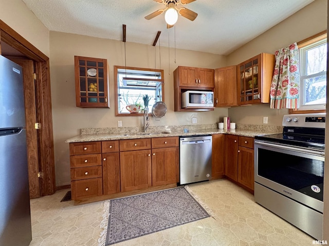 kitchen featuring light stone countertops, brown cabinetry, ceiling fan, a sink, and appliances with stainless steel finishes