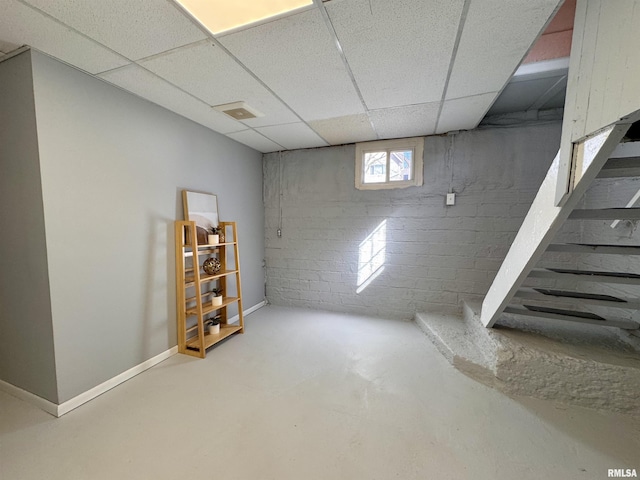 below grade area with concrete block wall, stairs, a paneled ceiling, and baseboards