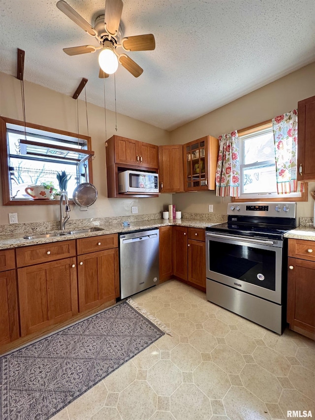 kitchen with glass insert cabinets, ceiling fan, brown cabinetry, stainless steel appliances, and a sink