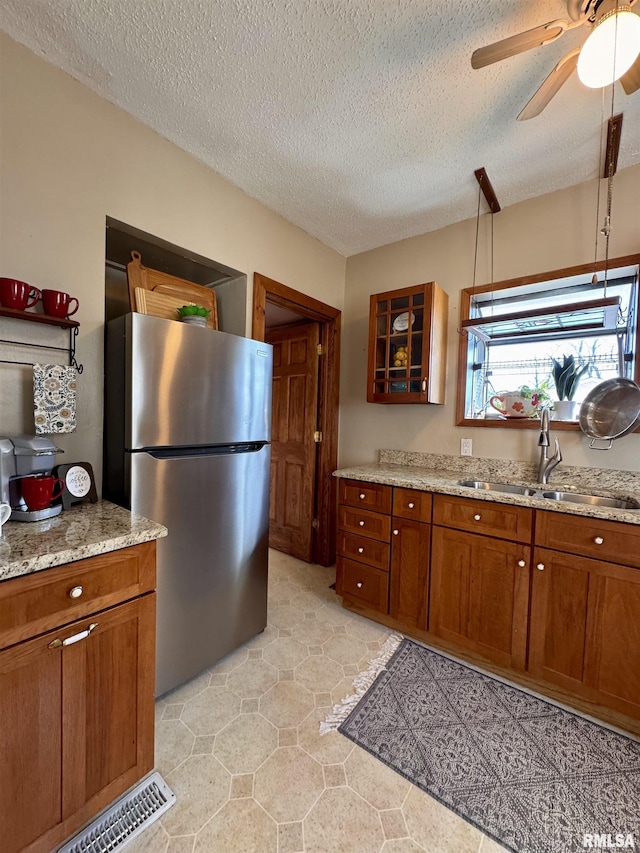 kitchen featuring brown cabinetry, freestanding refrigerator, and a sink