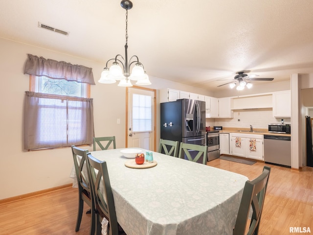 dining space with visible vents, light wood-style flooring, ceiling fan with notable chandelier, and baseboards