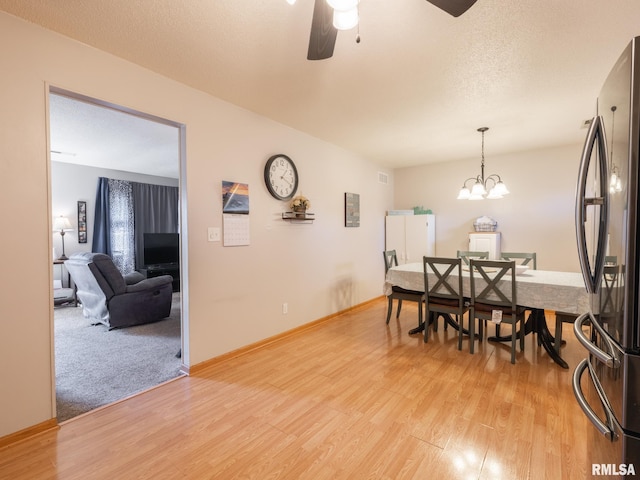 dining space with baseboards, ceiling fan with notable chandelier, light wood-type flooring, and a textured ceiling