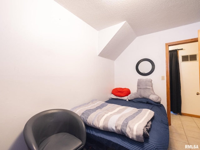 bedroom with vaulted ceiling, light tile patterned flooring, visible vents, and a textured ceiling