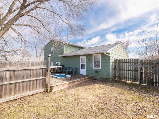 back of property with roof with shingles, a deck, and fence