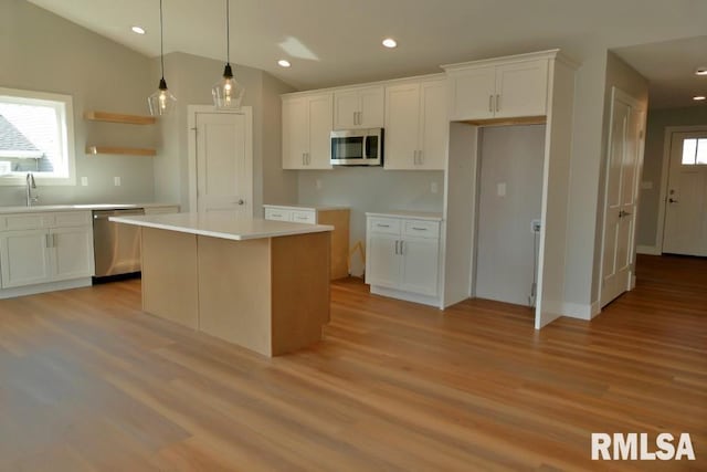 kitchen with stainless steel appliances, a kitchen island, light wood-style flooring, and white cabinetry