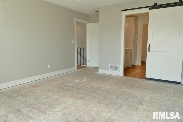 empty room with visible vents, a barn door, and baseboards