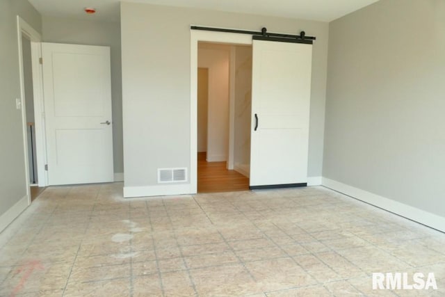 unfurnished bedroom featuring visible vents, baseboards, and a barn door